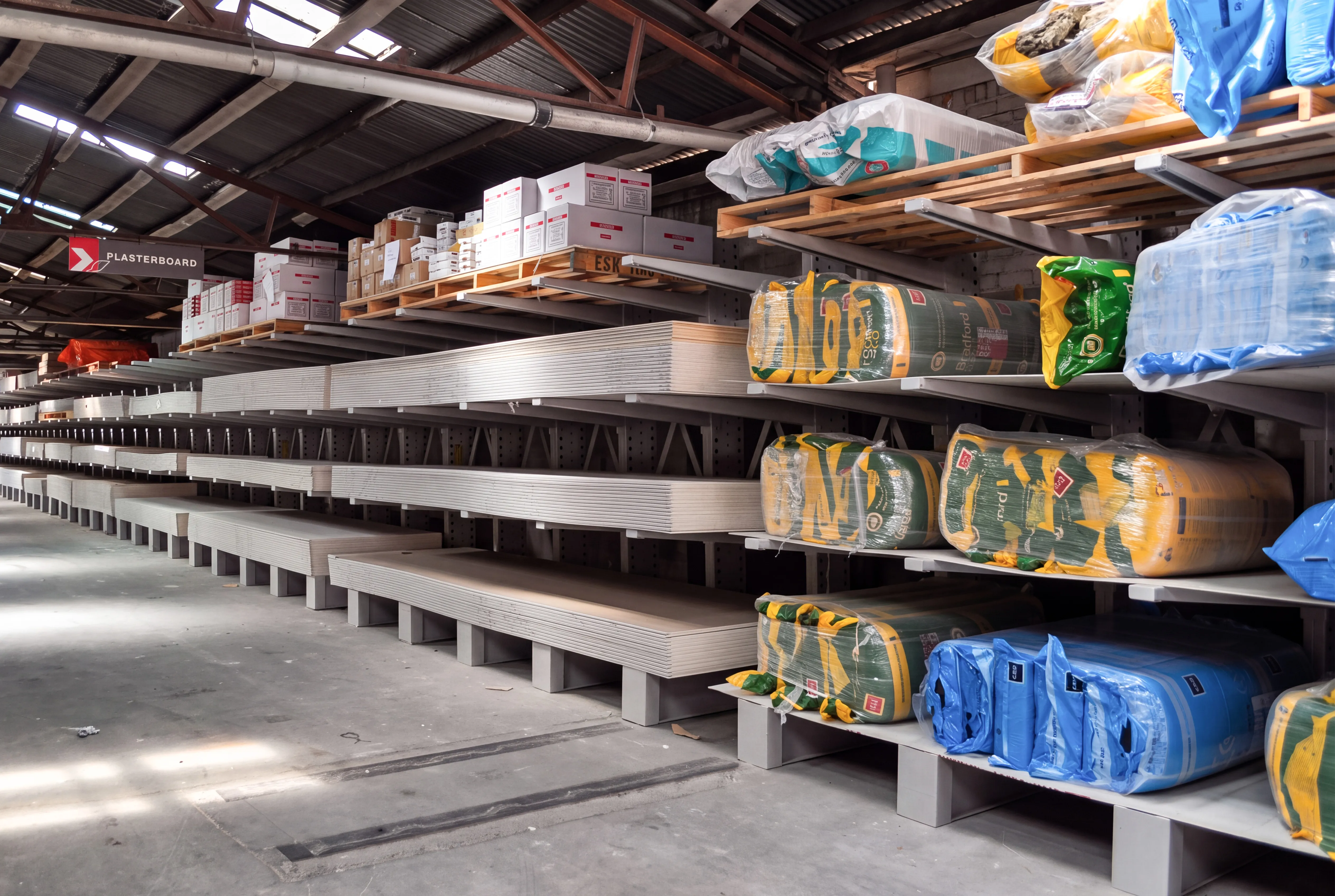 Warehouse shelves stocked with plasterboard sheets, insulation materials, and boxes under a metal roof. CSR Picton Hopkins Cantilever Racking