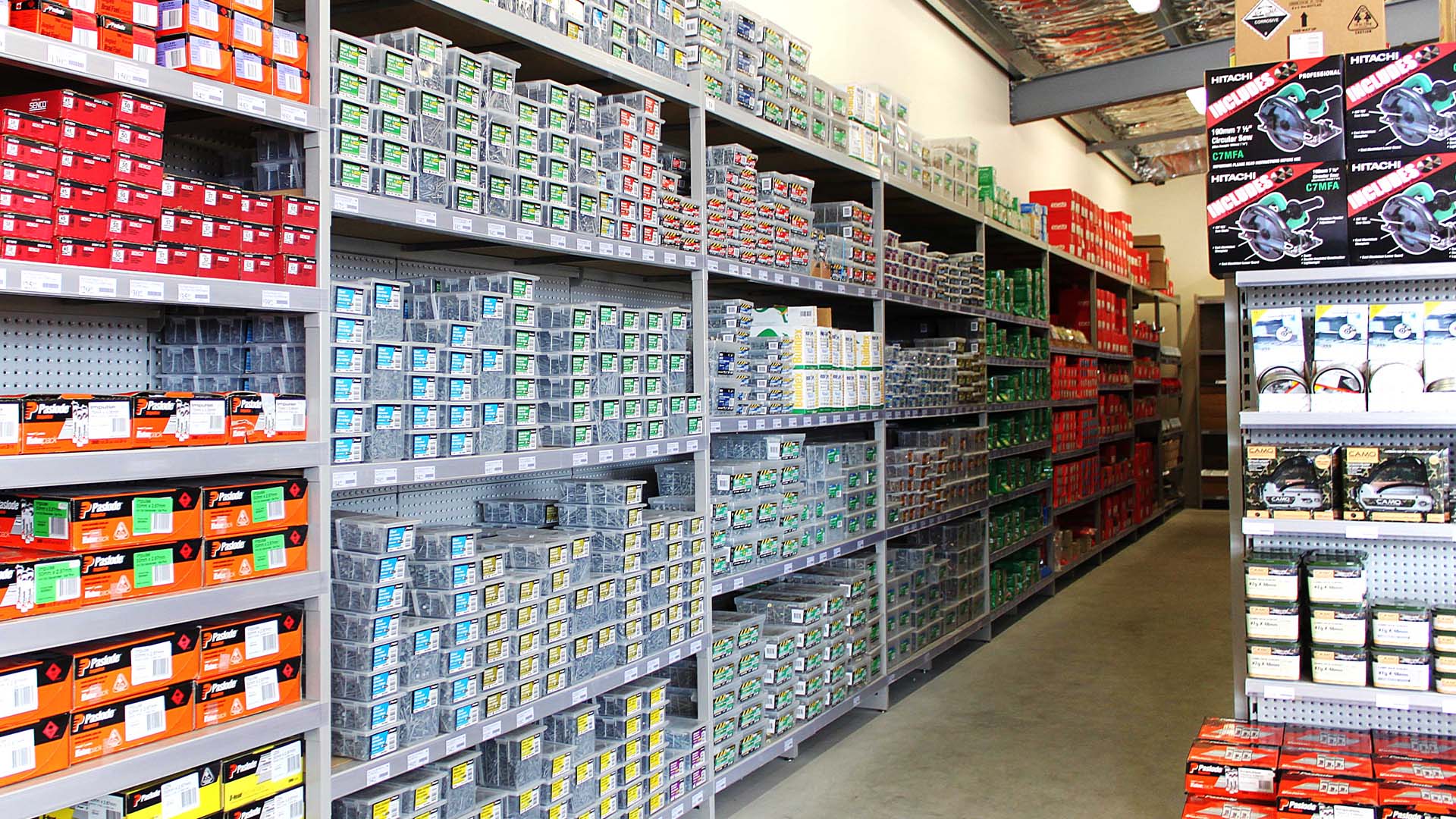 Aisle in a hardware store stocked with boxes of nails, screws, and fasteners on metal shelves.