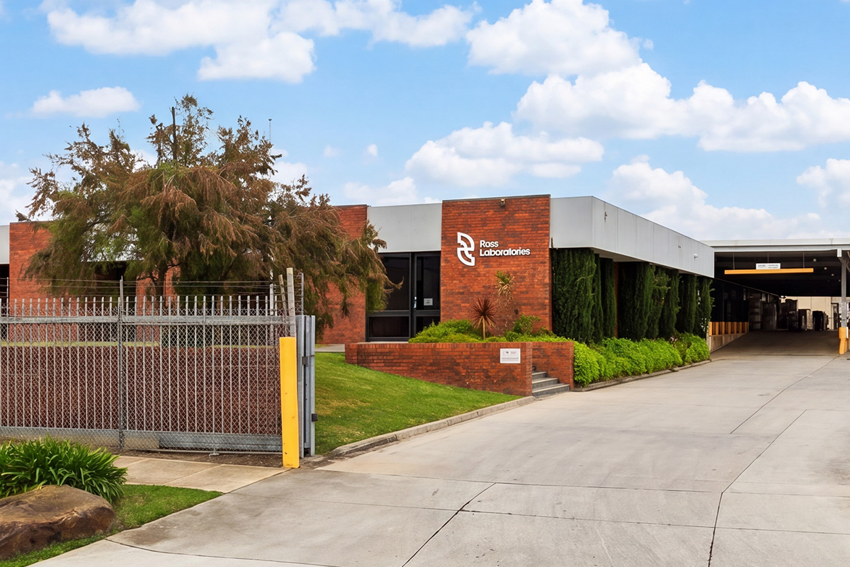 Entrance to Ross Laboratories with a brick building, greenery, and a gated fence under a partly cloudy sky.