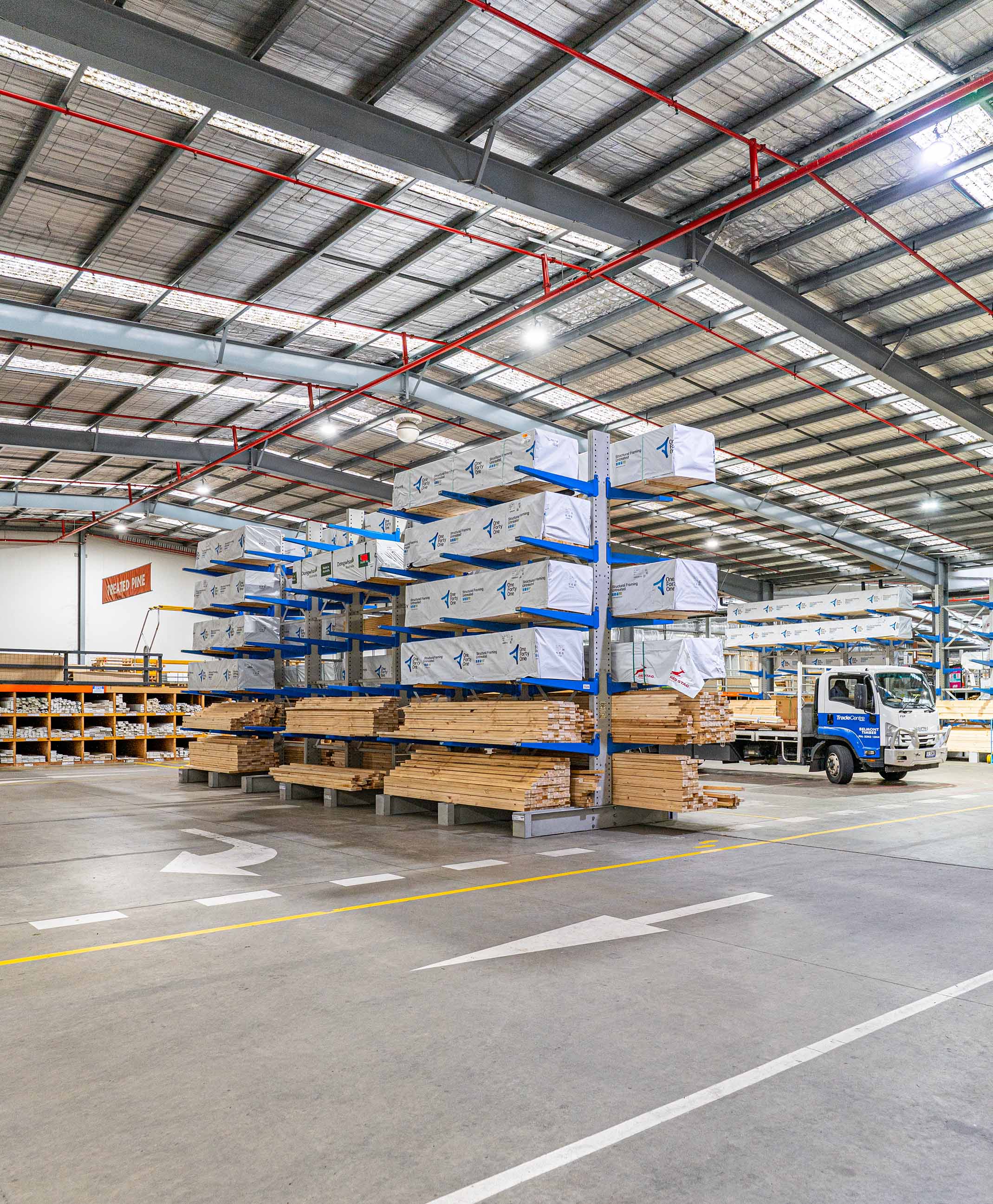 Warehouse interior with stacks of timber and wrapped lumber on blue racks and a white delivery truck.