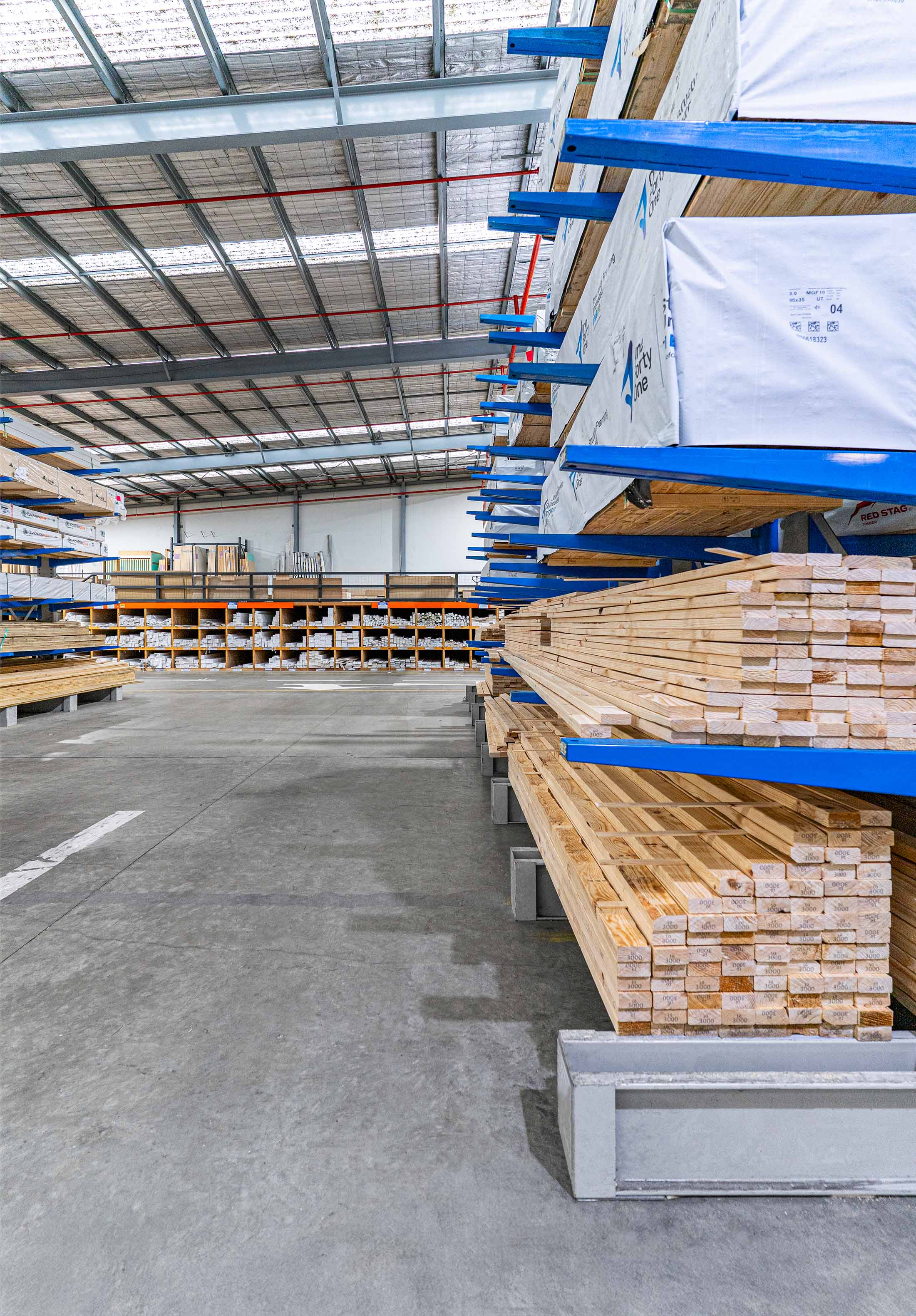 Warehouse interior with stacks of lumber held on blue metal cantilever racks and pigeon hole racking.