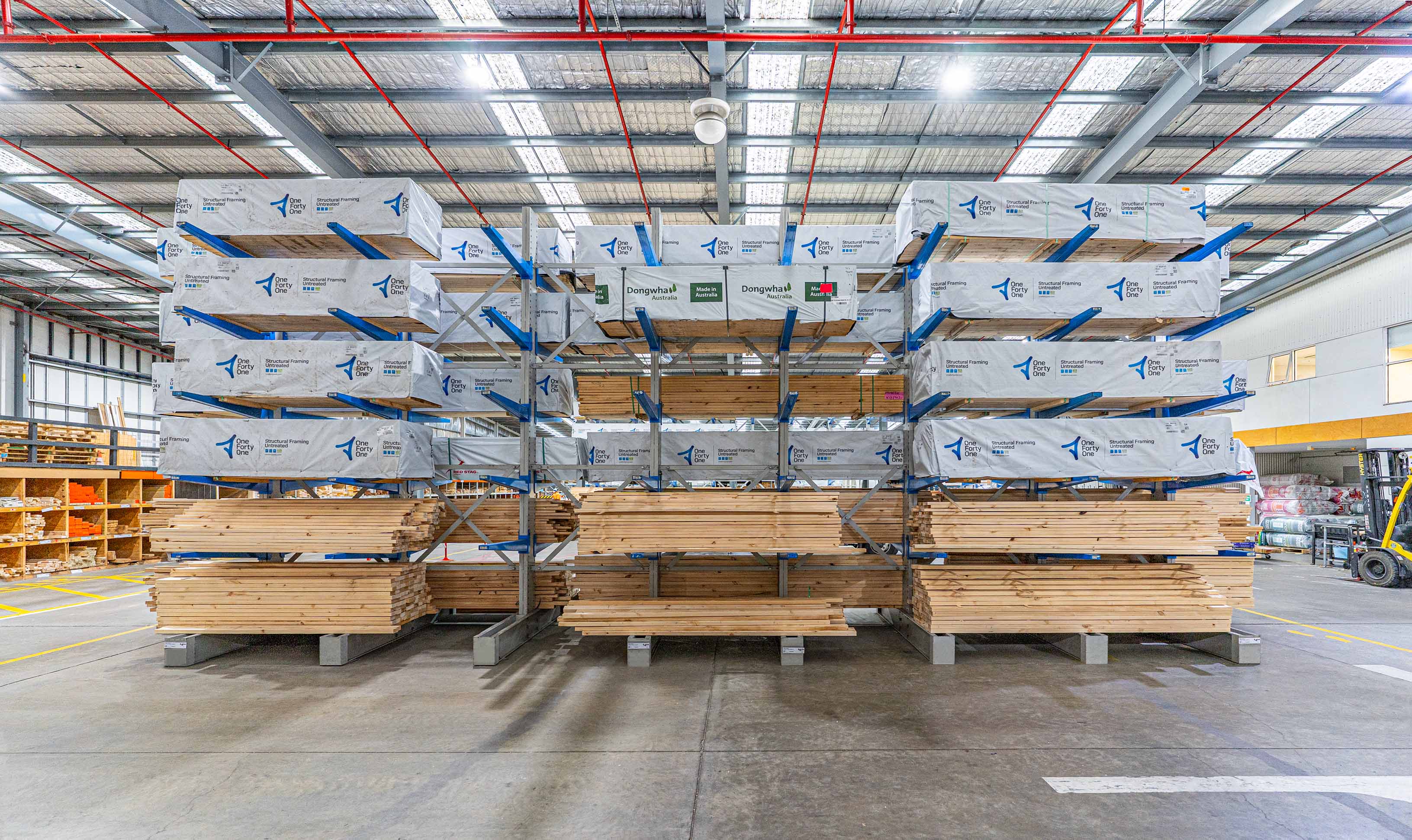 Wood planks stacked on blue cantilever racks inside a spacious warehouse with high ceilings.