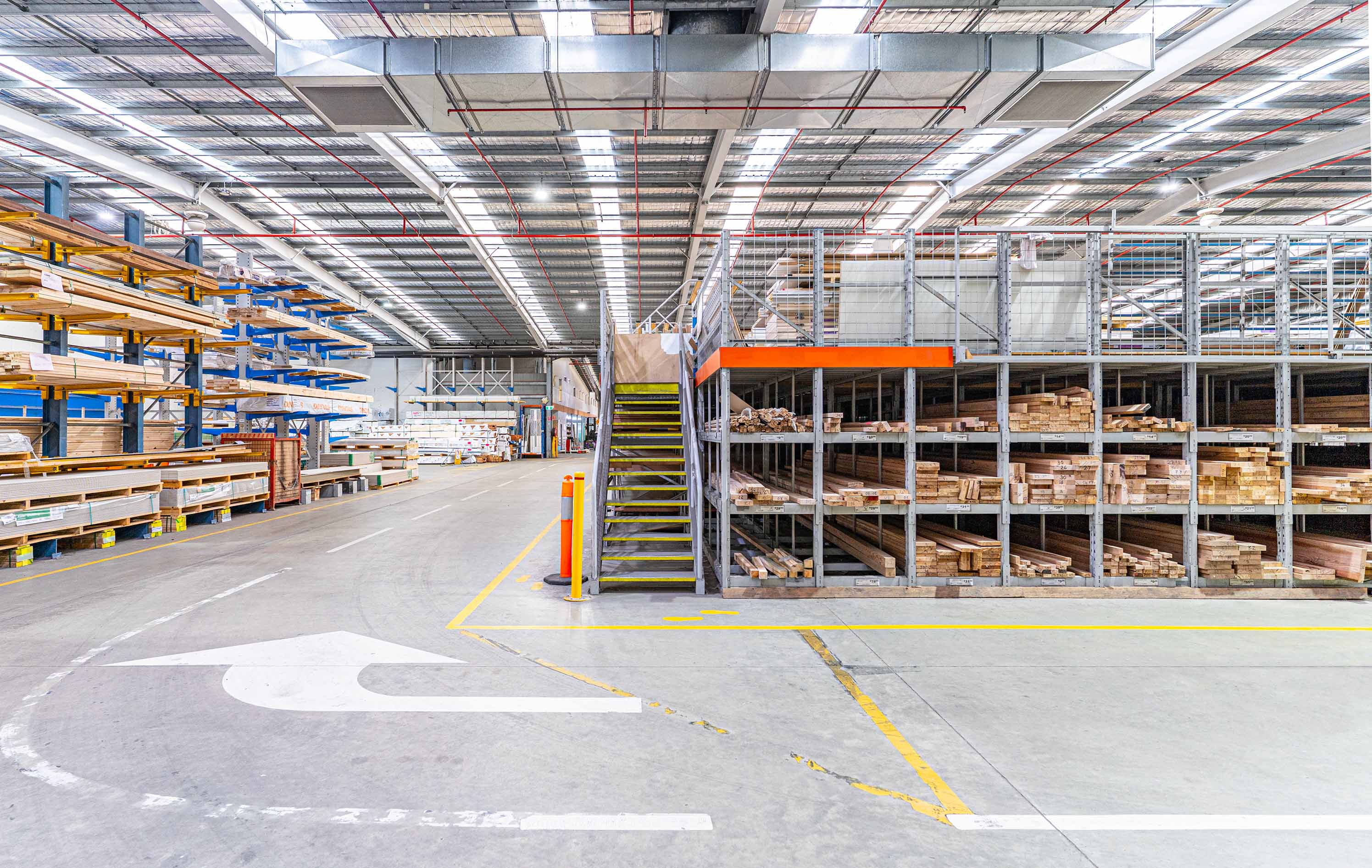 Interior view of a spacious lumber warehouse with cantilever racking, pigeon hole and mezzanine racking under bright lights.