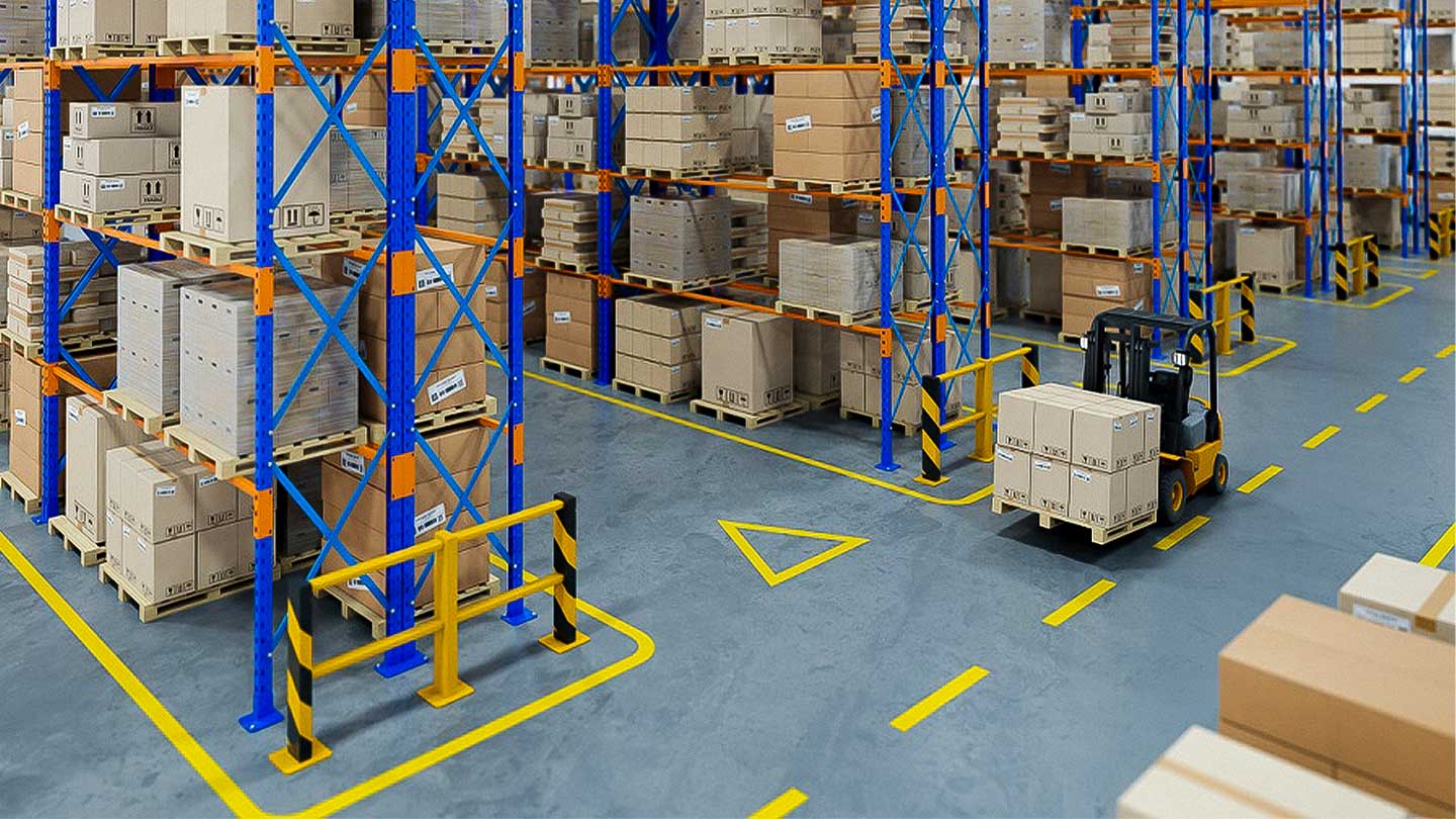 Forklift carrying stacked boxes in a warehouse aisle lined with blue and orange shelving holding numerous pallets of cardboard boxes.