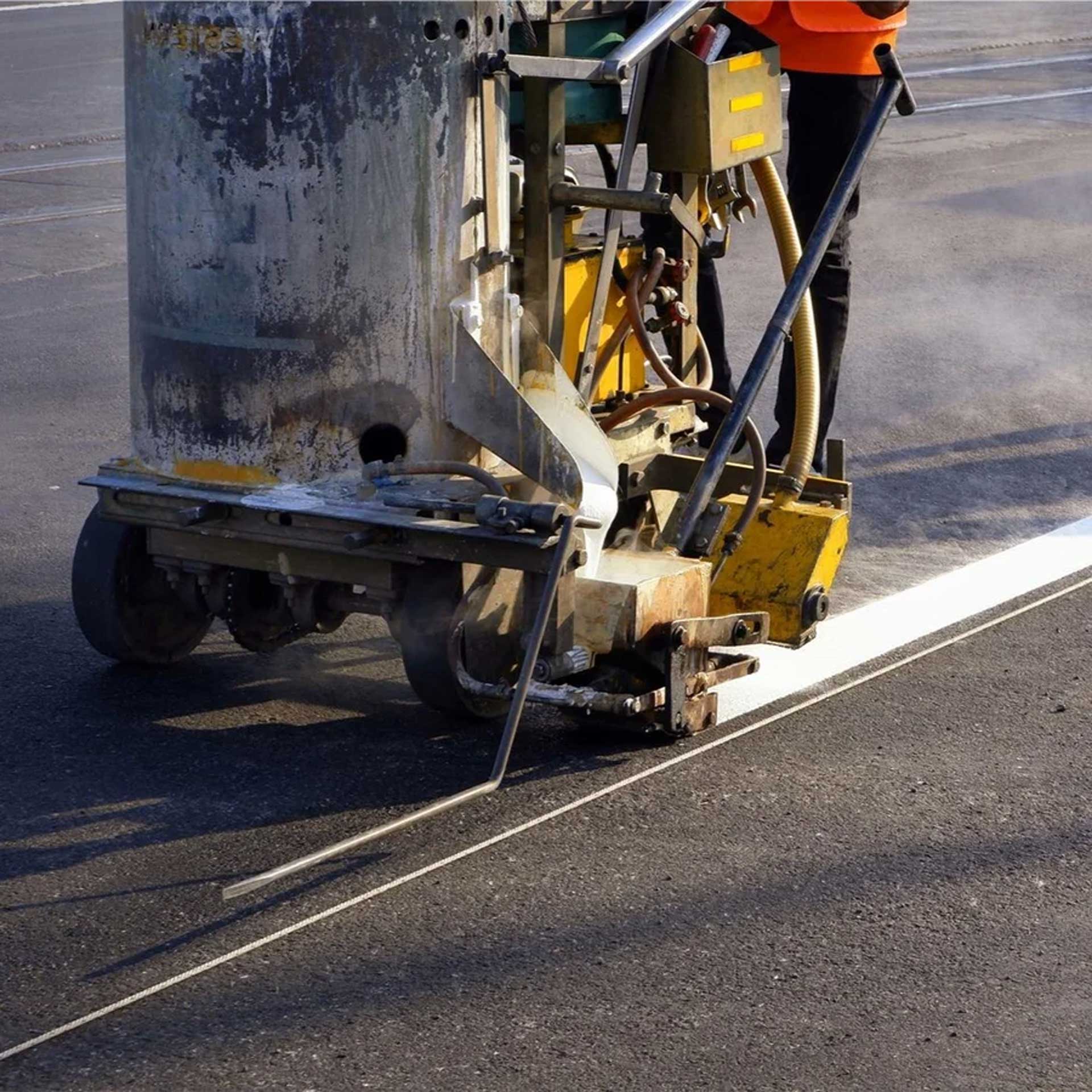 Close-up of a line marking machine painting a white line on asphalt.